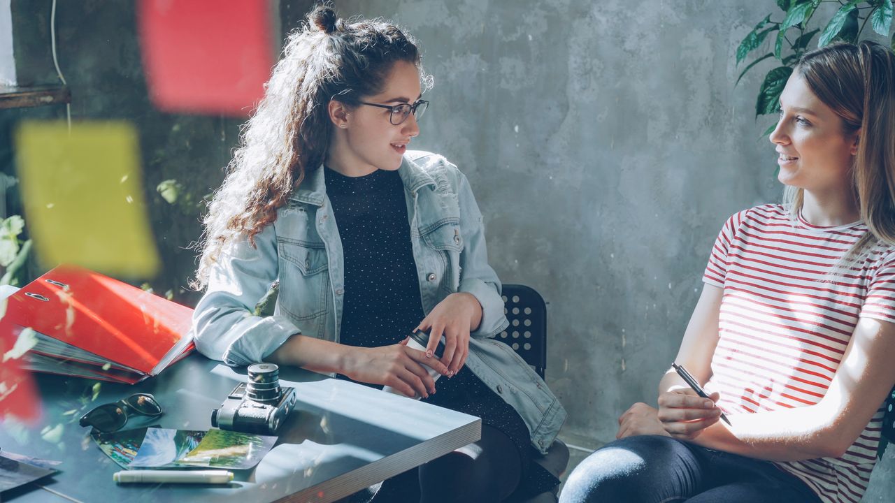 Two women engaging in conversation at a sunlit cafe table, creating a warm and inviting atmosphere.